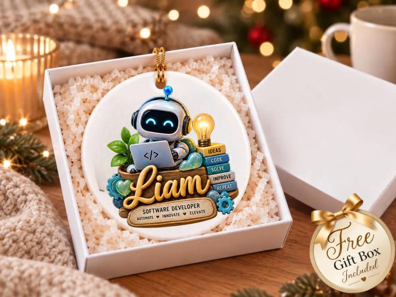 Może przedstawiać: Okrągła biała ceramiczna ozdoba przedstawiająca robota w słuchawkach, piszącego na laptopie z symbolem kodu. Imię Liam jest napisane złotą czcionką nad tekstem Software Developer, Automate, Innovate, Elevate.