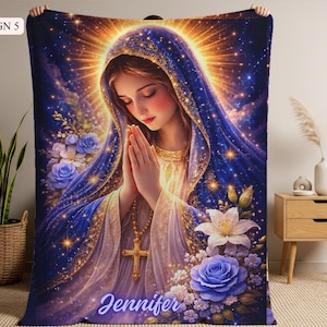 May include: A plush blanket featuring a serene illustration of a woman in prayer, adorned with a blue veil and gold accents. The design includes blue roses, white lilies, and the name "Jennifer". The blanket has a celestial theme.