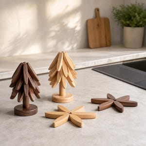Può includere: Due sculture in legno a forma di albero e due sottopentola piatti in legno a forma di stella. Un albero e un sottopentola sono realizzati in legno marrone scuro, mentre l'altro albero e il secondo sottopentola sono in legno chiaro.