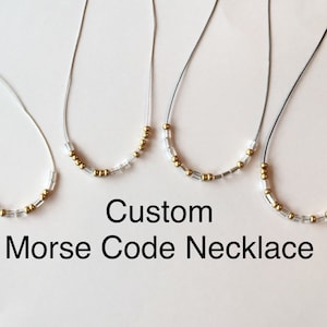 Op de afbeelding: Vier kettingen met een zilveren ketting en gouden kralen. De kettingen zijn in een rij gerangschikt, met de kortste ketting links en de langste ketting rechts. De kettingen bevinden zich op een witte achtergrond. De tekst "Custom Morse Code Necklace" staat onder de kettingen.