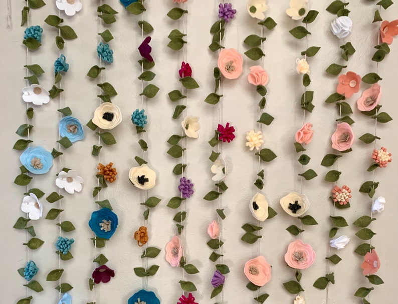 May include: A garland of felt flowers and leaves in various colors, including pink, blue, white, green, and brown. The garland is strung on a white string and is perfect for adding a touch of whimsy to any room.