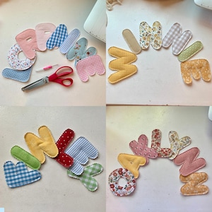 May include: A collection of colorful, fabric-covered letters in various patterns and colors, including floral, gingham, and polka dots. A pair of red scissors and a small pink tool are also present. The letters appear to be handmade.