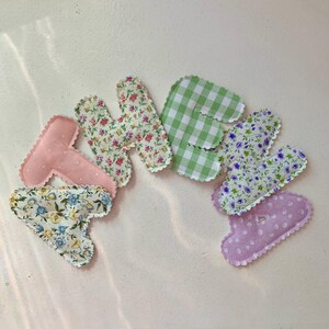 May include: A collection of fabric letters spelling "HEART". The letters are in various patterns, including floral prints, gingham, and polka dots. Each letter has a scalloped edge and is in shades of pink, green, and blue.