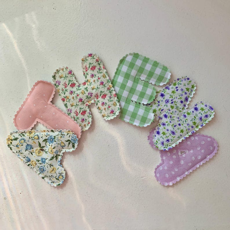May include: A collection of fabric letters spelling "HEART". The letters are in various patterns, including floral prints, gingham, and polka dots. Each letter has a scalloped edge and is in shades of pink, green, and blue.