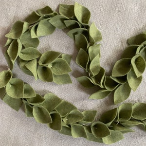 Puede incluir: Una guirnalda de fieltro verde hecha de hojas individuales, perfecta para añadir un toque de verdor a la decoración de tu hogar.