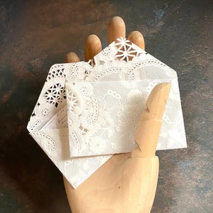May include: Two white lace doilies folded together in the shape of a house, held in a wooden hand.