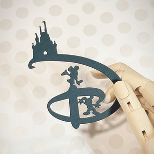 May include: A dark blue paper cutout of the Disney logo with a silhouette of Cinderella's castle and Mickey Mouse in the center.