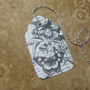 May include: A white gift tag with a black and white illustration of butterflies and flowers. The tag is tied with a black and white twine.