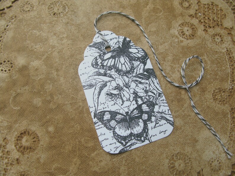 May include: A white gift tag with a black and white illustration of butterflies and flowers. The tag is tied with a black and white twine.