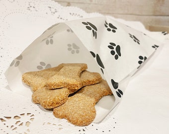 May include: A white paper bag with black paw print designs is filled with dog biscuits. The bag is sitting on a white doily.