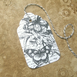 May include: A white gift tag with a black and white illustration of two butterflies and flowers. The tag is tied with a black and white twine.