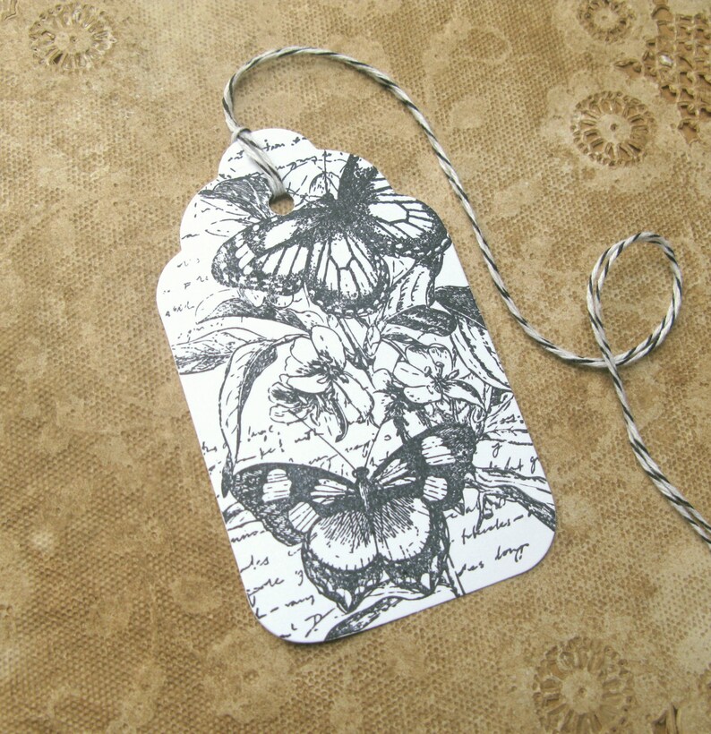 May include: A white gift tag with a black and white illustration of two butterflies and flowers. The tag is tied with a black and white twine.
