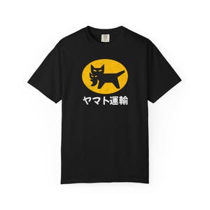 May include: Black t-shirt featuring a yellow oval with a black cat logo and Japanese text. The cat logo has a stylized design. The text below the logo is in white. The shirt is a basic crew neck.