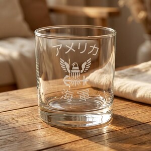 May include: A clear glass tumbler with etched Japanese text and a US Navy emblem. The tumbler features the words "America" and "Navy" in Japanese characters, along with an eagle, anchor, and other nautical symbols.