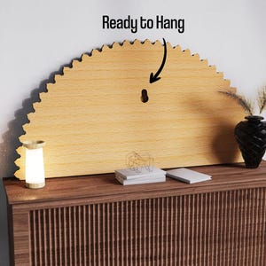 May include: A light-colored, semi-circular wooden wall decor piece with a scalloped edge. The text "Ready to Hang" is above the piece. A small, glowing lamp and a black vase with decorative plants are on a wooden cabinet.