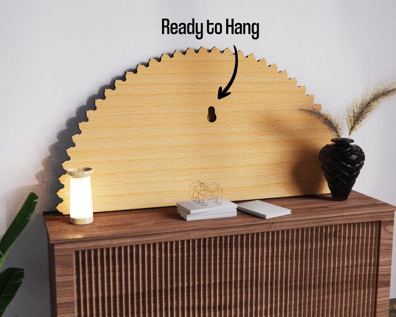 May include: A light-colored, semi-circular wooden wall decor piece with a scalloped edge. The text "Ready to Hang" is above the piece. A small, glowing lamp and a black vase with decorative plants are on a wooden cabinet.