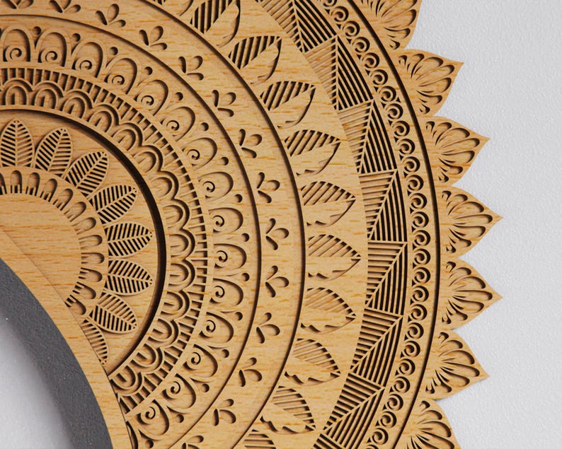 May include: Close-up of a wooden mandala with intricate, laser-cut patterns. The design features concentric circles with floral and geometric elements. The wood has a natural, light brown color, and the details are finely etched.
