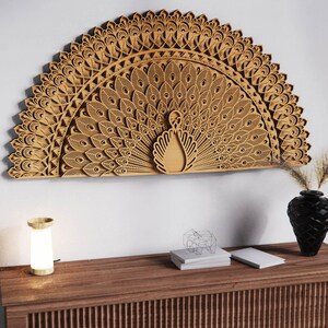May include: A large, intricately carved wooden peacock wall art piece. The peacock's fanned tail is the focal point, with detailed feather patterns. The artwork is mounted on a white wall above a wooden cabinet with a lamp, vase, and decorative items.