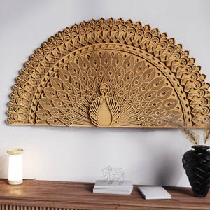 May include: A large, intricately carved wooden peacock wall art piece. The artwork features a detailed fan-shaped design with layered feathers and a central peacock figure. The piece is mounted on a white wall above a wooden console table.