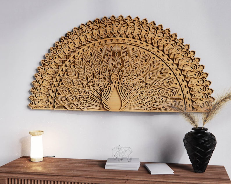 May include: A large, intricately carved wooden peacock wall art piece. The artwork features a detailed fan-shaped design with layered feathers and a central peacock figure. The piece is mounted on a white wall above a wooden console table.