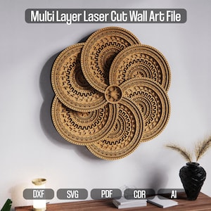 Op de afbeelding: Multi Layer Laser Cut Wall Art File. Een groot, gelaagd houten wandkunstwerk in een bloemenontwerp. Het kunstwerk is gemaakt van meerdere cirkelvormige stukken met ingewikkelde patronen. Het stuk is aan een witte muur bevestigd. Een zwarte vaas met gedroogde planten staat op een houten tafel.