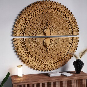 May include: Two-piece, laser-cut wooden wall art depicting a peacock with its tail feathers fanned out. The artwork is a light brown color and features intricate details. The peacock's body is in the center of the design. The artwork is mounted on a white wall.