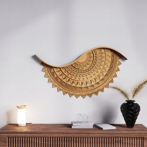 May include: A large, intricately carved wooden wall hanging in a wave shape, featuring detailed geometric patterns. The piece is a light brown color and is mounted on a white wall. A black vase with dried plants sits on a wooden cabinet below.
