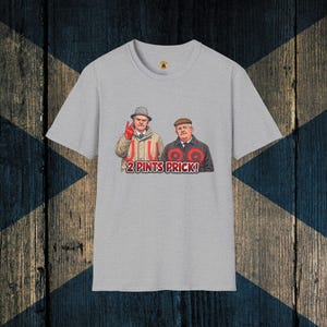 Puede incluir: Camiseta gris claro con una ilustración de dibujos animados de dos hombres y el texto "2 Pints Prick!". Los hombres llevan sombreros y abrigos. Uno hace el signo de la paz. La camiseta tiene cuello redondo y mangas cortas.