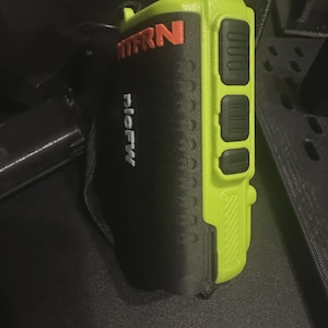 May include: A two-way radio with a black and neon green color scheme. The radio has the text "MFRN" in orange and the text "plcFW" in white. The radio has three black buttons on the side.