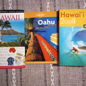 May include: Three travel guide books for Hawaii. The books feature colorful covers with images of beaches, surfing, and palm trees. Titles include "Hawaii," "Oahu," and "Hawaii 2008."