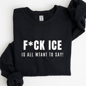 May include: Black sweatshirt with the text "F*CK ICE IS ALL WTANT TO SAY!" in white block letters. The sweatshirt is folded neatly on a white surface. The Gildan brand tag is visible.