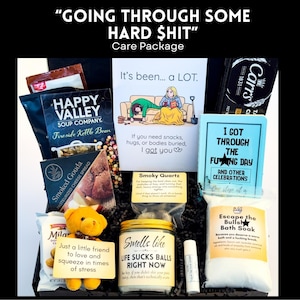 May include: A care package containing a Happy Valley soup mix, Carr's crackers, Smoked Gouda cheese spread, a yellow teddy bear, a candle labeled 'Smells Like Life Sucks Balls Right Now', bath soak, and cards with text including 'Going Through Some Hard Shit'.