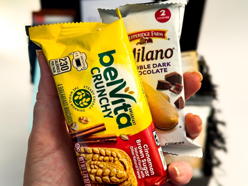 Op de afbeelding: Een gele verpakking belVita Crunchy Cinnamon Brown Sugar ontbijtkoekjes en een witte verpakking Pepperidge Farm Milano Double Dark Chocolate koekjes. De belVita-verpakking toont 230 calorie&euml;n en 4 koekjes, terwijl de Milano-verpakking 2 koekjes toont.