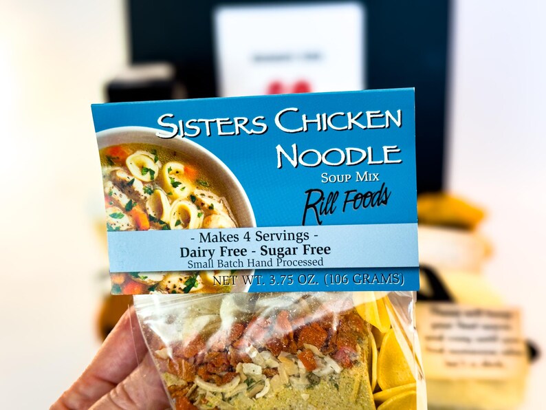 Puede incluir: Un paquete de mezcla para sopa de fideos con pollo Sisters. La etiqueta azul muestra el nombre del producto, una imagen de sopa y el texto "Makes 4 Servings - Dairy Free - Sugar Free". Peso neto: 106 gramos.
