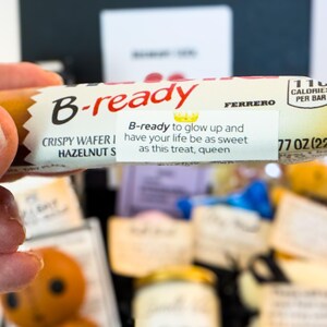 Puede incluir: Una oblea crujiente B-ready con relleno de avellanas se sostiene en una mano. El envoltorio dice "B-ready" en rojo, con el texto "B-ready to glow up and have your life be as sweet as this treat, queen." Contiene 110 calor&iacute;as por barra y pesa 22g.