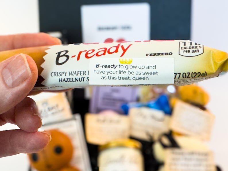 Puede incluir: Una oblea crujiente B-ready con relleno de avellanas se sostiene en una mano. El envoltorio dice "B-ready" en rojo, con el texto "B-ready to glow up and have your life be as sweet as this treat, queen." Contiene 110 calor&iacute;as por barra y pesa 22g.