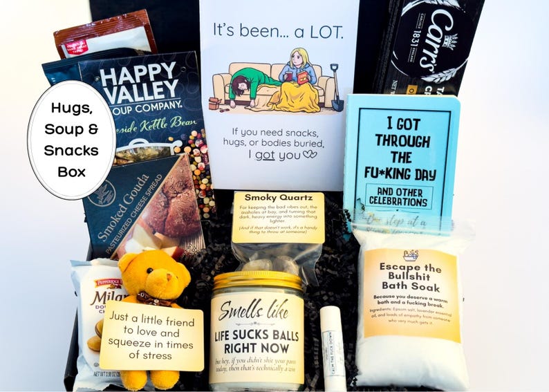 Op de afbeelding: Een geschenkdoos met Happy Valley soepmix, Carr's crackers, Smoked Gouda kaasspread, een gele teddybeer, een kaars met het label Smells like LIFE SUCKS BALLS RIGHT NOW, lippenbalsem en een zakje Escape the Bullshit badzout.