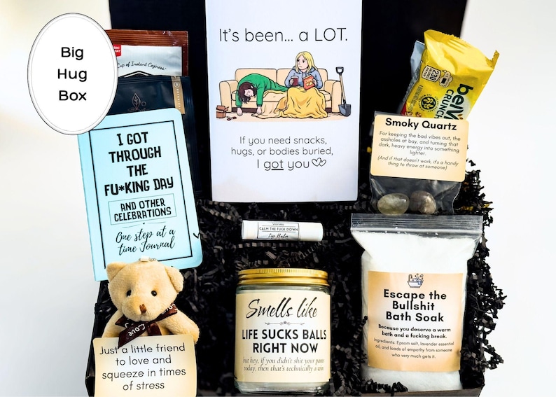 Op de afbeelding: Een geschenkdoos met een dagboek getiteld I Got Through The F*cking Day, een wenskaart met een cartoon, een kleine teddybeer met een briefje, een kaars met het label Smells Like Life Sucks Balls Right Now, badzout, lippenbalsem en rookkwartsstenen.