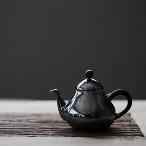 Pode incluir: Uma chaleira de prata com uma pega preta e um botão preto na tampa. A chaleira está sobre uma superfície de madeira.