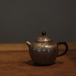Pode incluir: Uma chaleira de prata com uma pega de madeira e uma tampa redonda. A chaleira está sobre uma mesa de madeira.