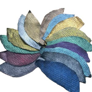 May include: A collection of fish skin leather pieces arranged in a fan shape, featuring a variety of iridescent and metallic colors including gold, silver, blue, green, purple, and teal, each displaying a distinct, repeating scale pattern.