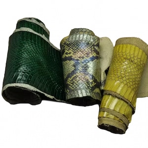May include: Three rolled pieces of textured material. The left piece is a deep emerald green with a rectangular scale pattern. The center piece features a multi-colored snakeskin print with yellow, black, and grey tones. The right piece is bright yellow.
