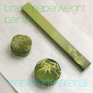 May include: A set of three olive green brass paperweights featuring gold-colored botanical illustrations. The collection includes one long rectangular bar and two circular pieces, all decorated with detailed bamboo and floral motifs in a matte finish.