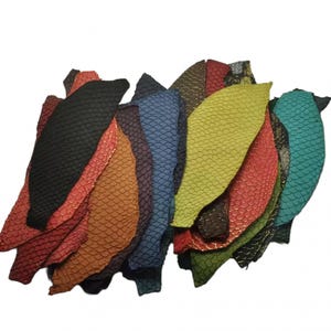 May include: A collection of irregularly shaped leather scraps featuring a distinct embossed scale pattern. The pieces are dyed in a variety of vibrant colours including black, red, orange, purple, blue, lime green, and teal, with visible texture.