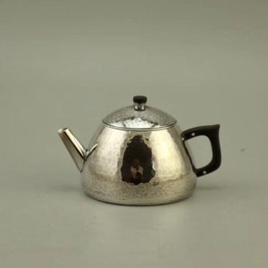 Pode incluir: Uma chaleira de prata com acabamento martelado e uma alça preta. A chaleira tem um corpo redondo e uma tampa com uma pequena pega.
