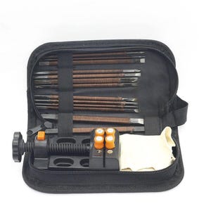May include: A black zippered carrying case containing a set of metal tools with brown textured handles, a black mechanical vise with orange adjustment knobs, and a folded off-white cloth, all organized within elastic loops and compartments.