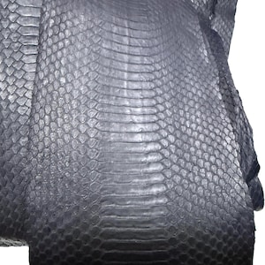 Peut inclure: Une peau de serpent bleu marine foncé présentant un motif distinct de grandes écailles rectangulaires le long du centre, flanquées d'écailles plus petites et arrondies sur les côtés. Le matériau a une finition lisse, semi-brillante et souple.