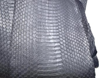 May include: A dark navy blue snakeskin hide featuring a distinct pattern of large, rectangular scales running down the center, flanked by smaller, rounded scales on the sides. The material has a smooth, semi-glossy finish and a flexible texture.