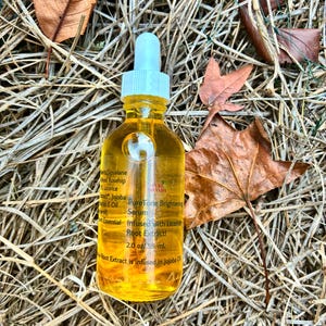 May include: A clear glass bottle filled with a yellow liquid, featuring a white dropper and a white cap. The bottle is labeled "PureTone Brightening Serum" and "Infused with Licorice Root Extract!" The bottle contains 2.0 oz / 59 ml. The bottle is surrounded by dry leaves and grass.