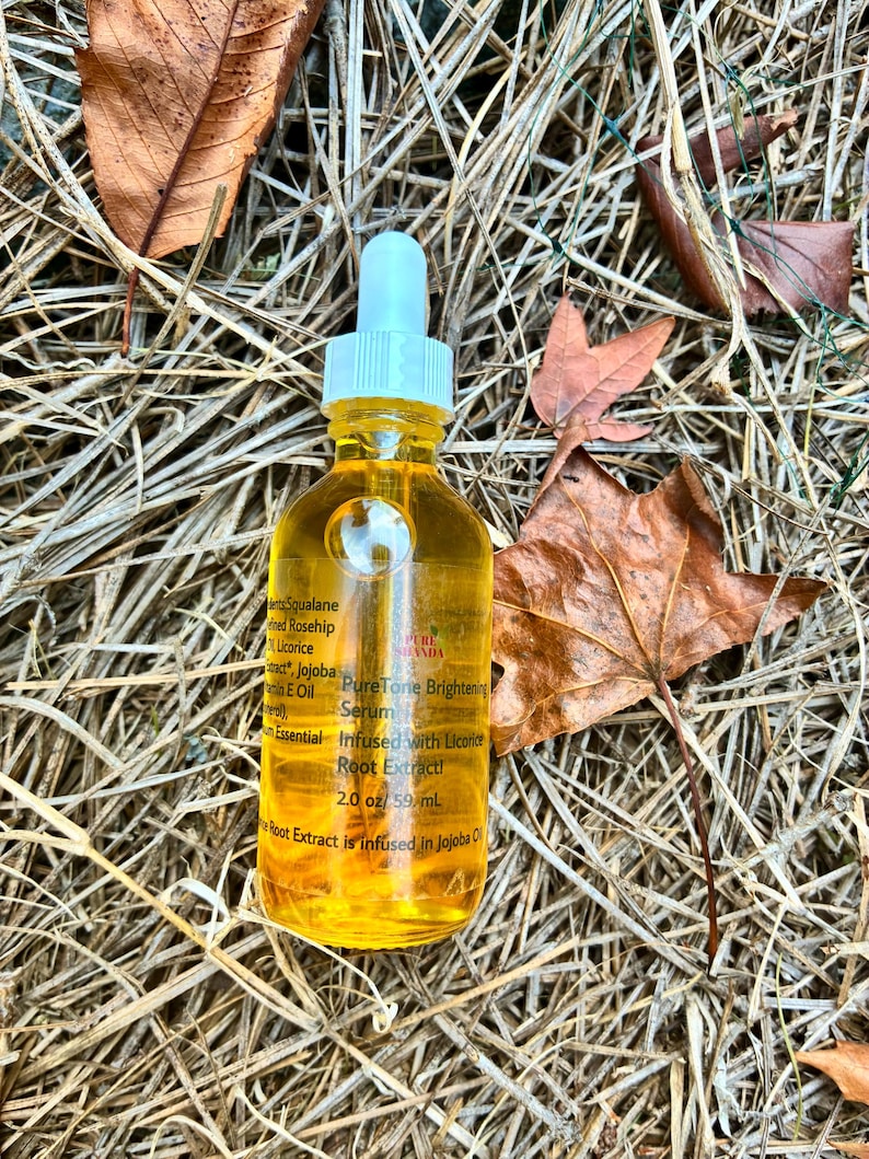 May include: A clear glass bottle filled with a yellow liquid, featuring a white dropper and a white cap. The bottle is labeled "PureTone Brightening Serum" and "Infused with Licorice Root Extract!" The bottle contains 2.0 oz / 59 ml. The bottle is surrounded by dry leaves and grass.